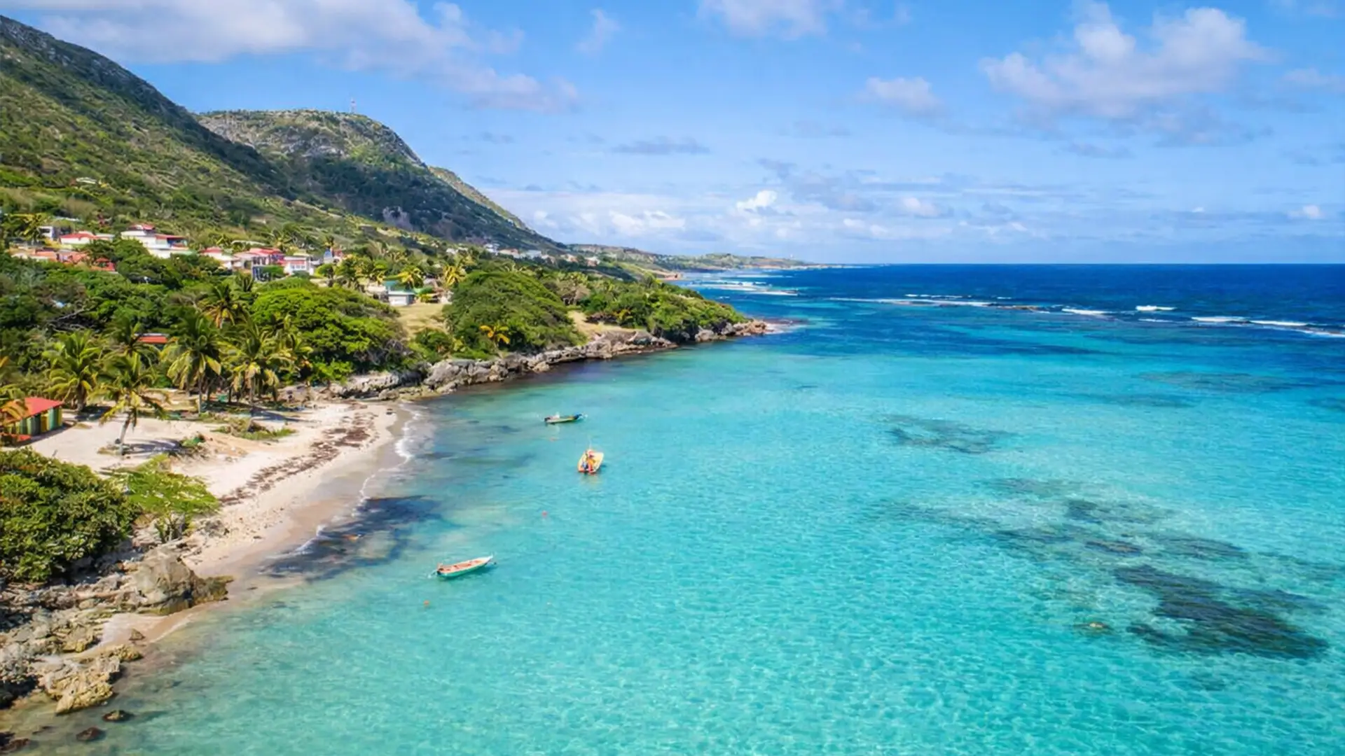 Littoral de La Désirade en Guadeloupe, avec plage de sable clair, eau turquoise et collines verdoyantes en arrière-plan.