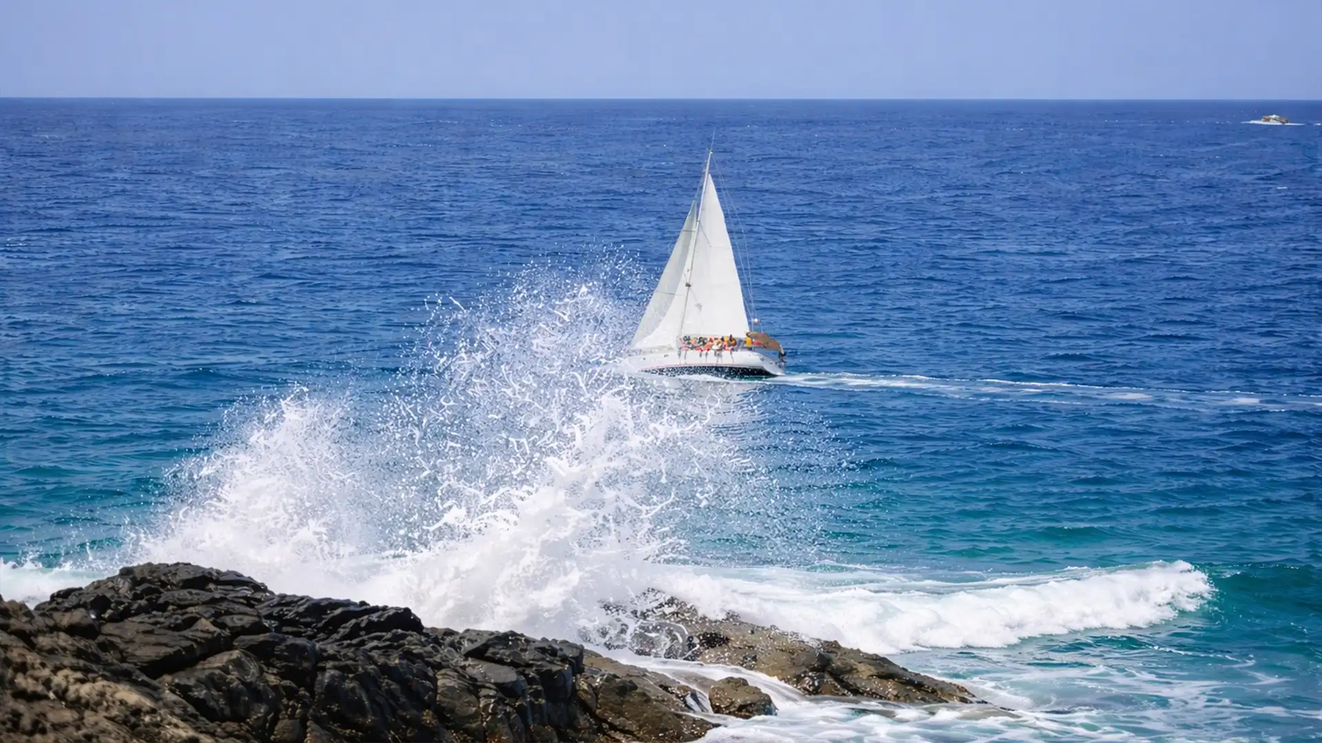 Excursion Les Saintes en voilier au départ de Rivière-Sens en Guadeloupe, bateau à voile naviguant sur une mer turquoise avec vagues sur la côte rocheuse
